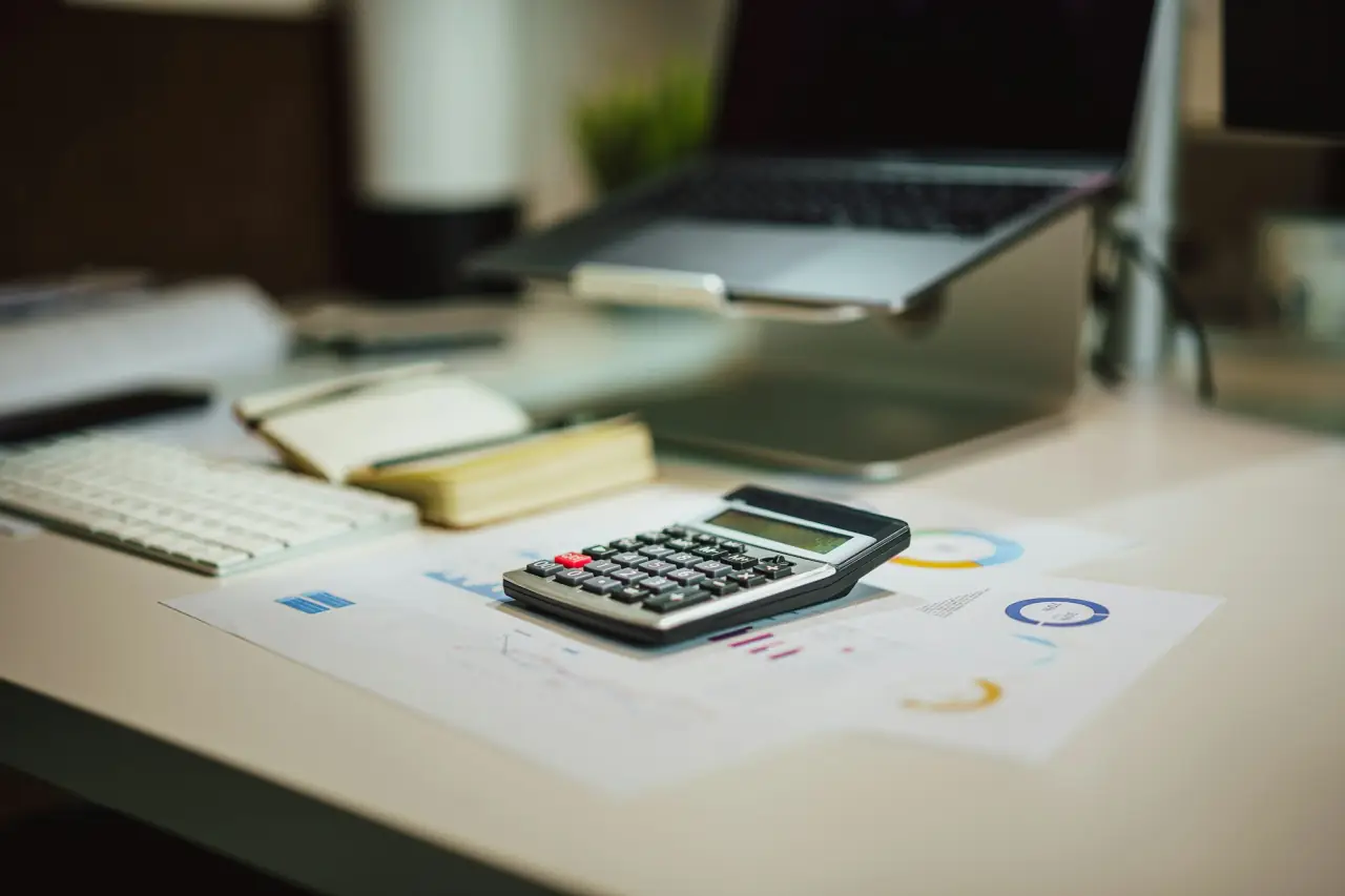Calculator and printed charts on a desk next to a laptop